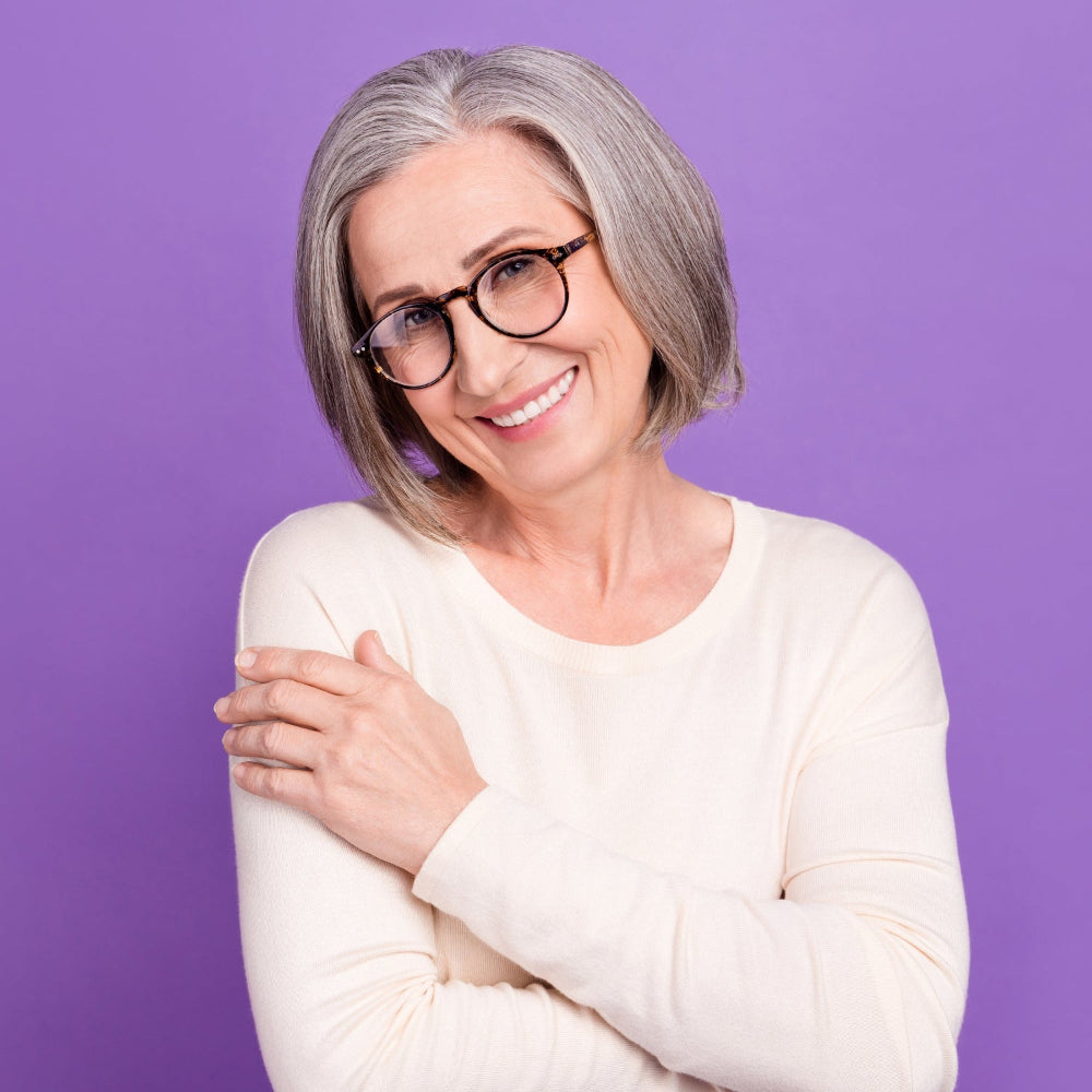 Woman with gray hair and glasses smiling against a purple background