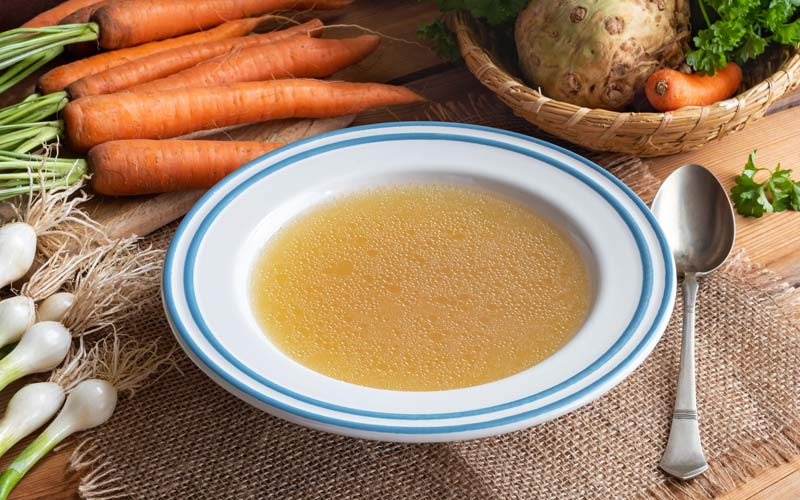 Bowl of Homemade Chicken Bone Broth Soup with Veggies on Table - Happy Healthy You